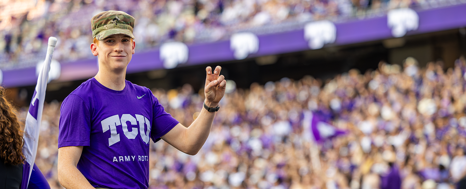 TCU ROTC student at a football game throwing up the go frogs hand sign 