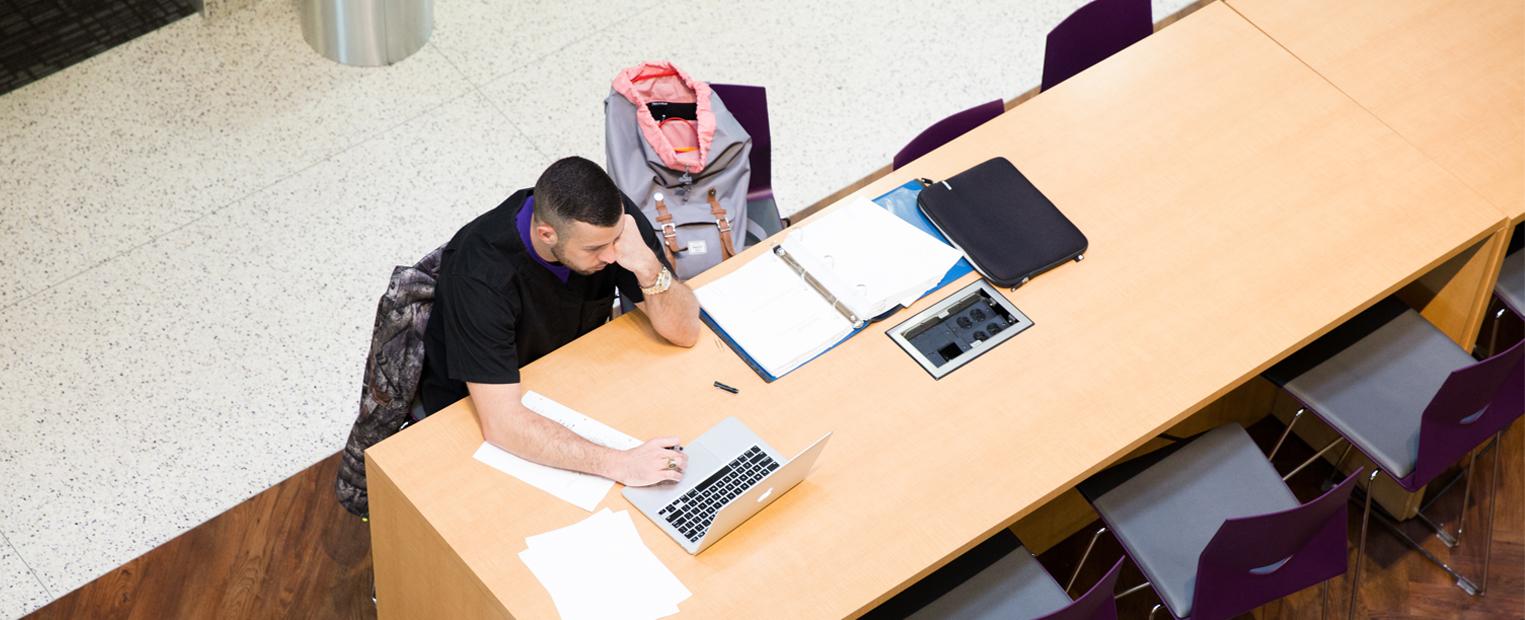 Student studying with books and a laptop in the Bass Building