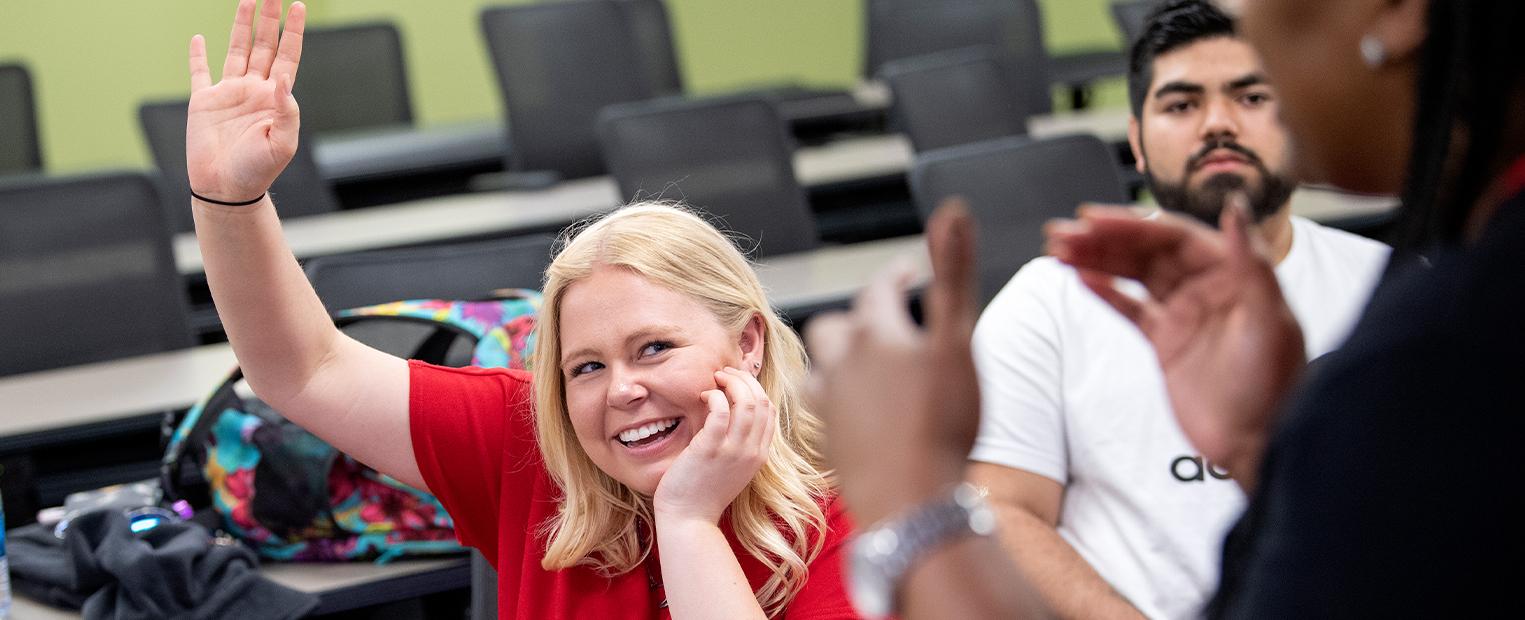 female student smiling while raising hand 