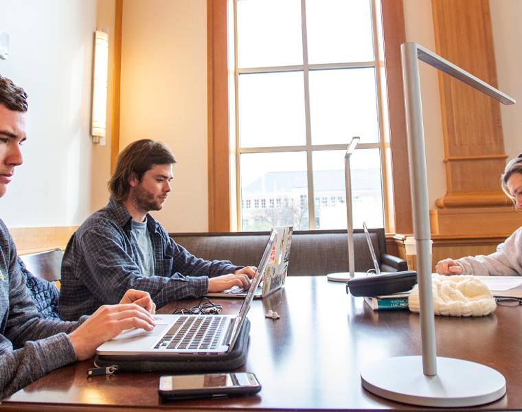 Two male and one female students sharing a table while studying in a common area on campus 