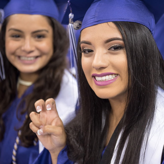 Happy graduate smiles while showing the frog sign