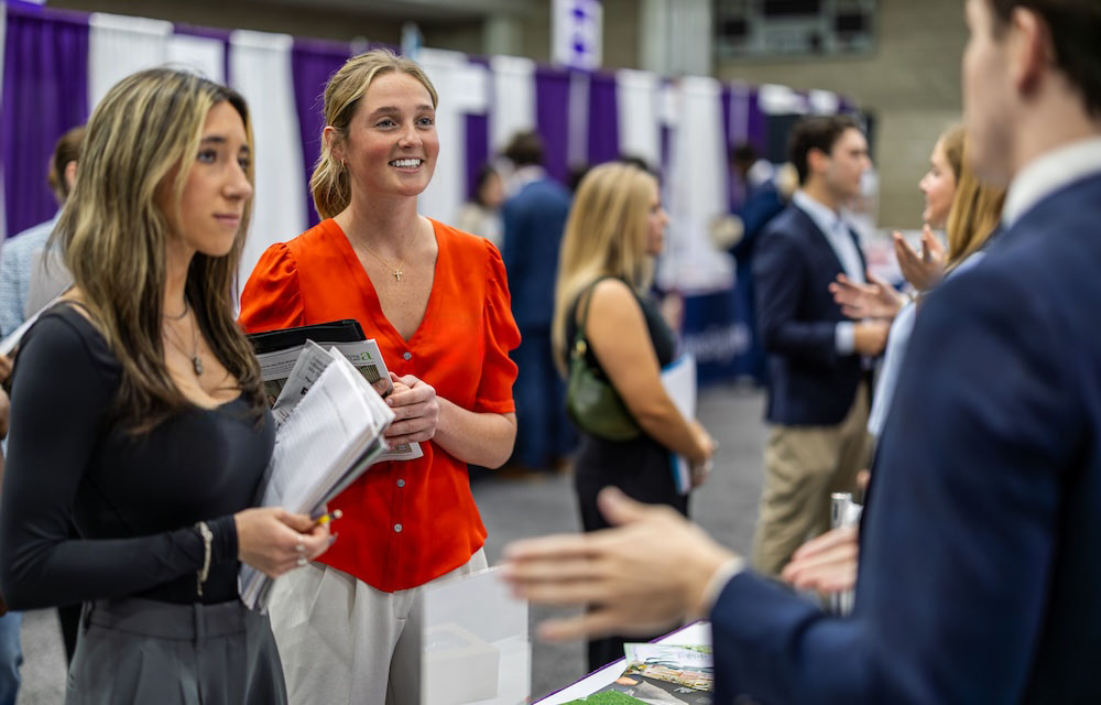Two students speak to employer representative at career fair