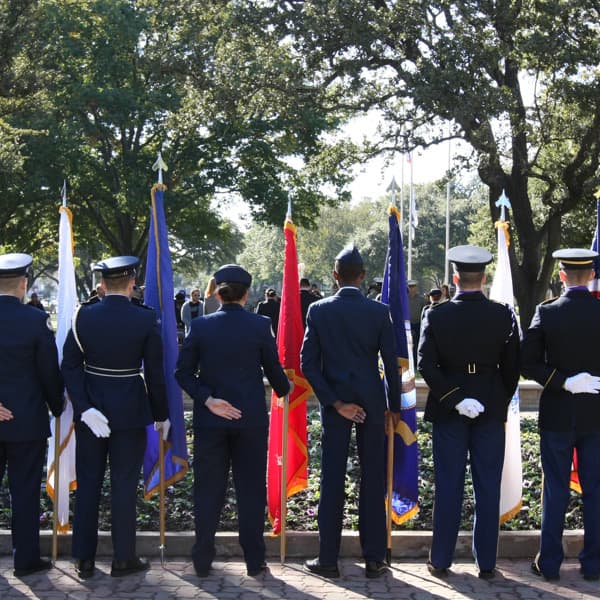 the backs of men and women in uniform standing closely together holding flags